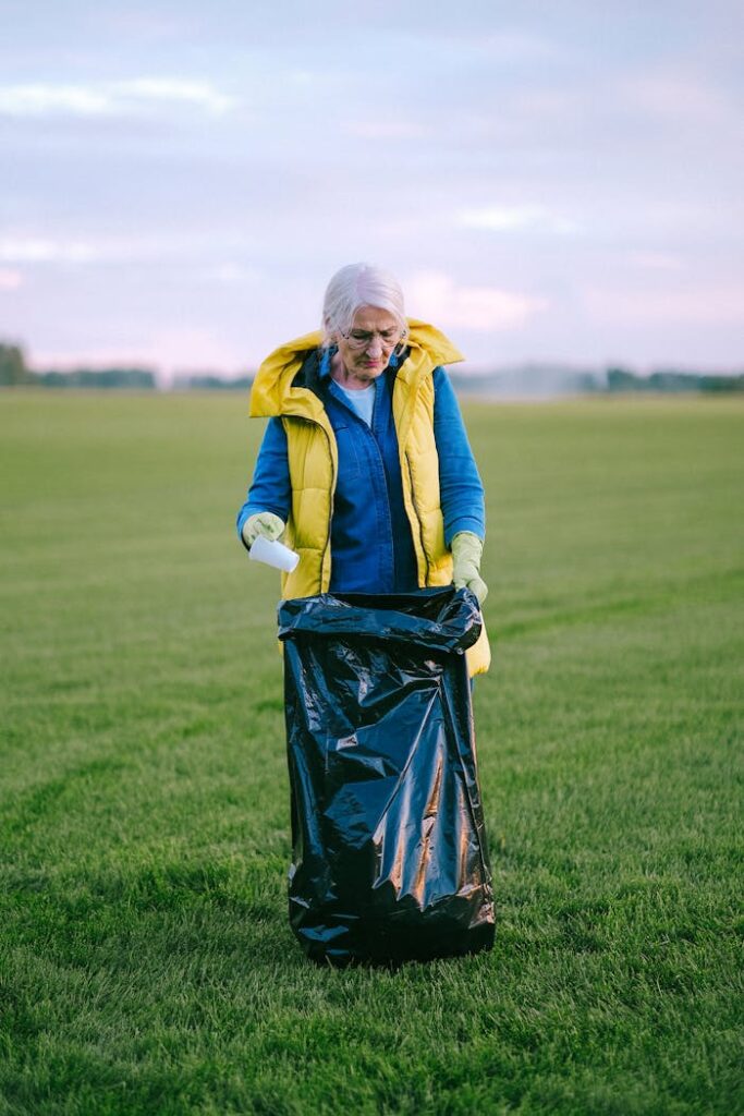 An elderly woman volunteering and collecting trash in a lush green field, promoting environmental care.