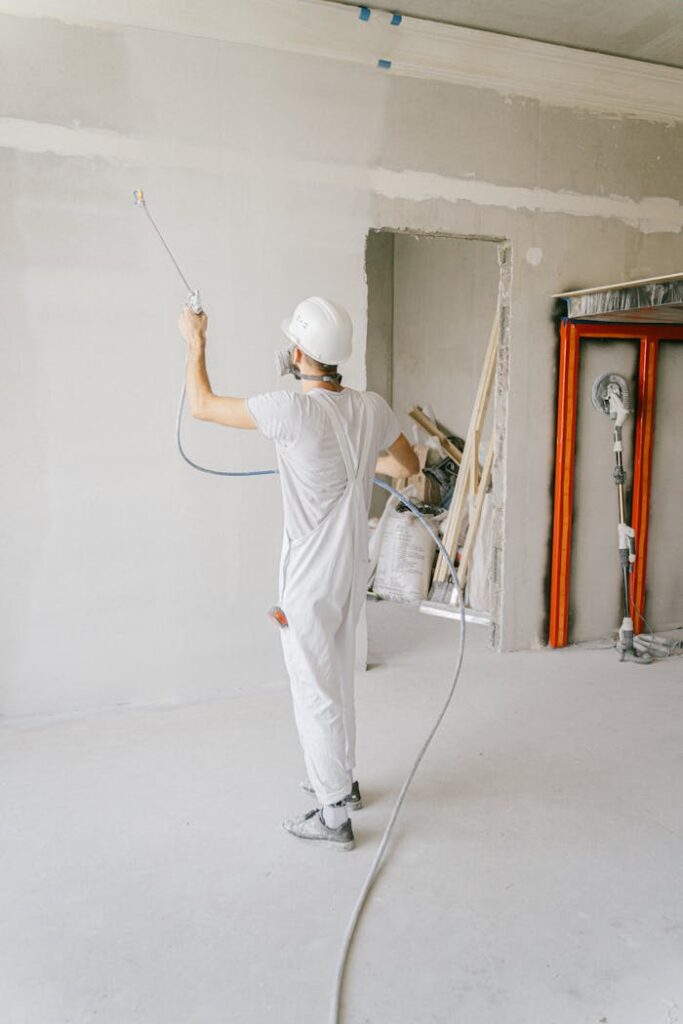 Back view of a construction worker applying primer to a wall in a renovation project indoors.