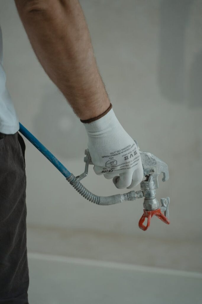 Arm of a worker holding a spray gun wearing gloves in an indoor setting, ready for painting.